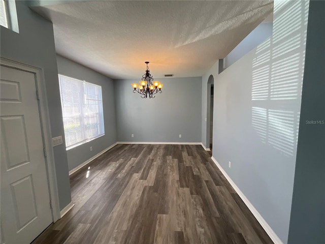 unfurnished dining area featuring visible vents, baseboards, dark wood-style floors, arched walkways, and a textured ceiling