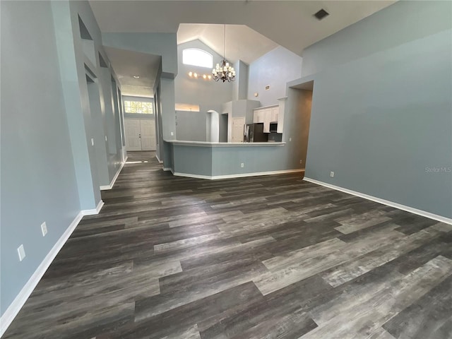 unfurnished living room featuring dark wood finished floors, a notable chandelier, baseboards, and high vaulted ceiling