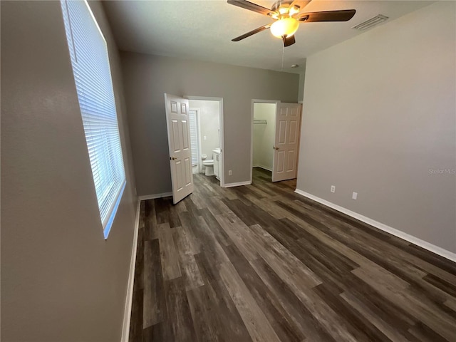 unfurnished bedroom with visible vents, a walk in closet, dark wood-type flooring, ensuite bathroom, and baseboards