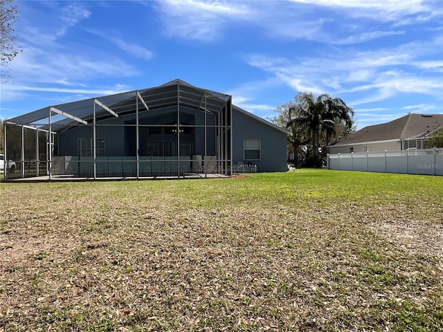 rear view of house featuring a lanai, a lawn, and fence