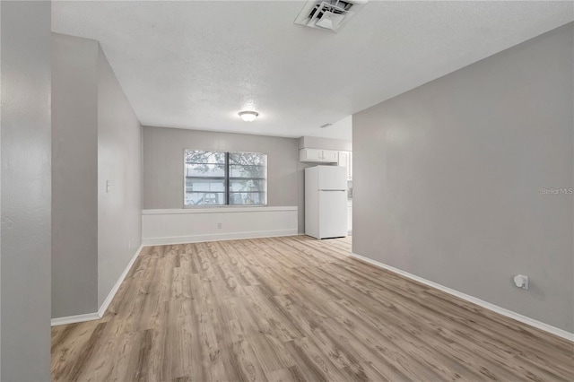 unfurnished living room featuring light wood-style flooring, baseboards, visible vents, and a textured ceiling