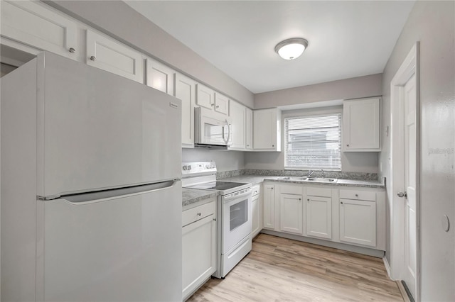 kitchen featuring light wood finished floors, light countertops, white cabinets, white appliances, and a sink