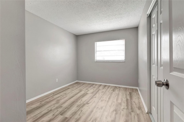 unfurnished room featuring light wood-type flooring, baseboards, and a textured ceiling