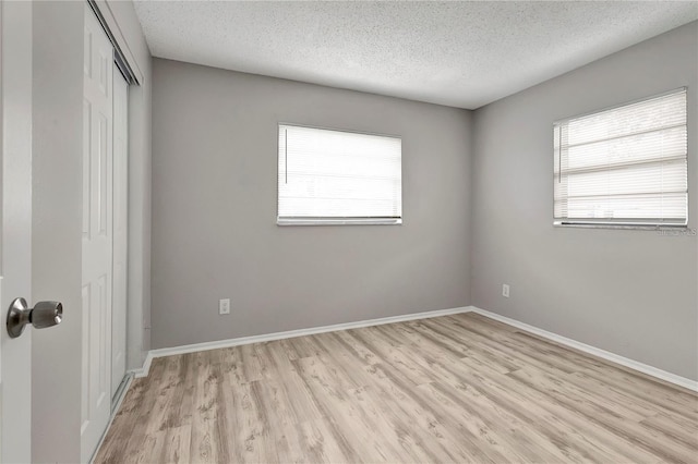 unfurnished bedroom featuring baseboards, light wood-style floors, a closet, and a textured ceiling