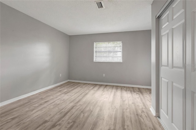 unfurnished bedroom featuring visible vents, a textured ceiling, baseboards, and light wood-style floors