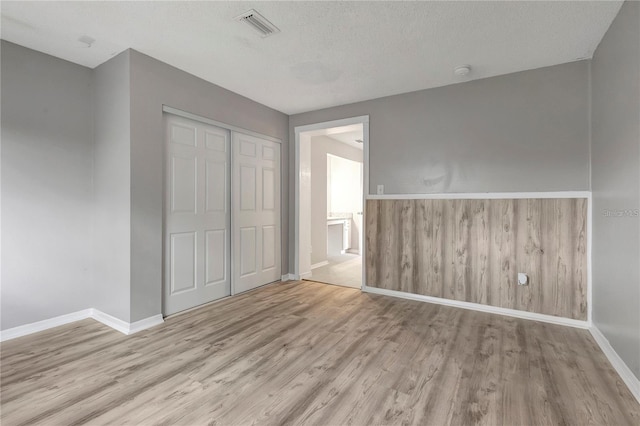 unfurnished bedroom with wood finished floors, visible vents, a closet, and baseboards