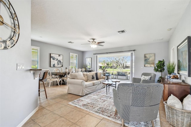 living room with light tile patterned floors, visible vents, baseboards, and ceiling fan