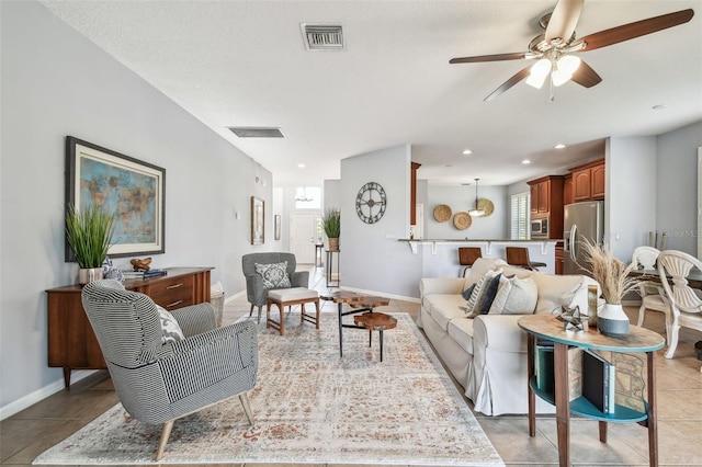 living room featuring light tile patterned flooring, visible vents, baseboards, and a ceiling fan