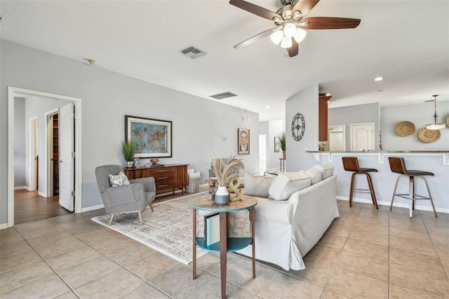 living area featuring light tile patterned floors, visible vents, baseboards, and ceiling fan