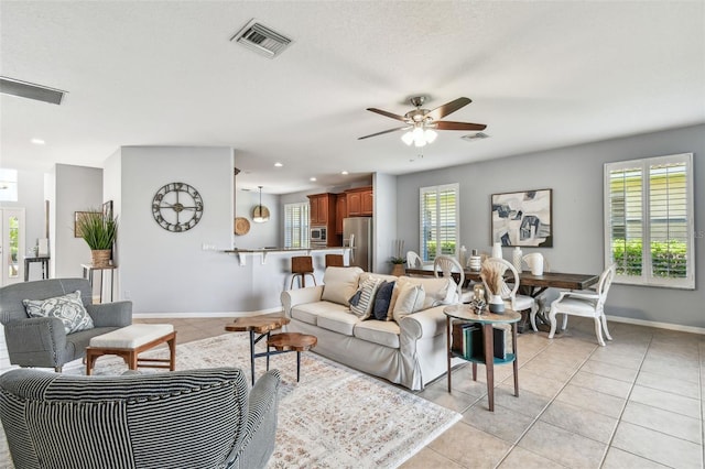 living room with light tile patterned floors, visible vents, baseboards, and ceiling fan