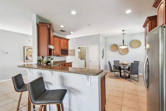 kitchen with visible vents, a peninsula, light tile patterned flooring, freestanding refrigerator, and a kitchen breakfast bar