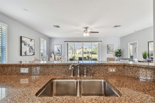 kitchen featuring visible vents, dark stone countertops, a ceiling fan, and a sink