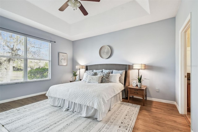 bedroom with a ceiling fan, a raised ceiling, wood finished floors, and baseboards