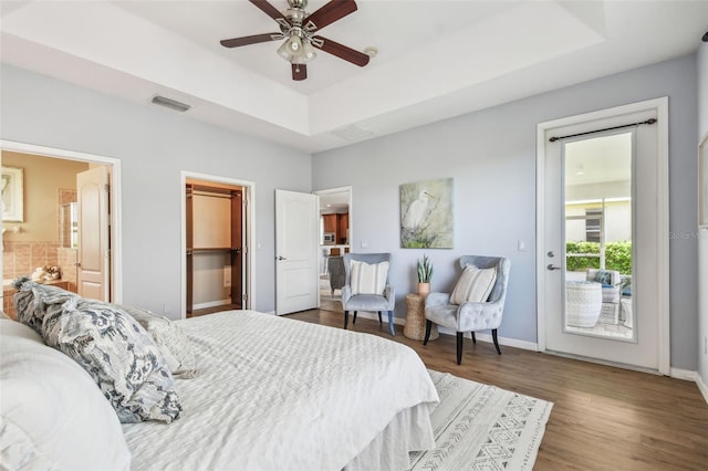 bedroom with wood finished floors, visible vents, baseboards, a tray ceiling, and access to exterior