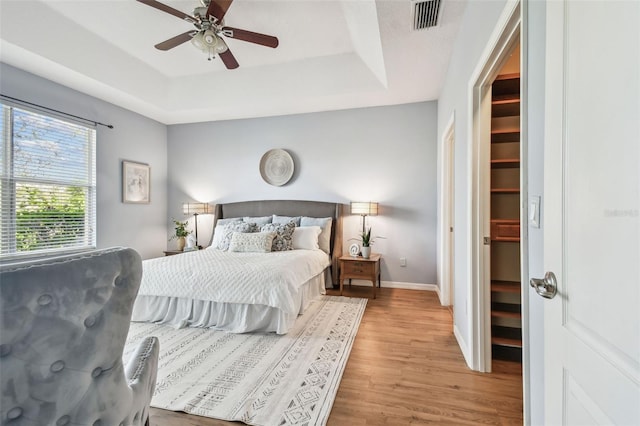 bedroom with visible vents, light wood-type flooring, a raised ceiling, and baseboards