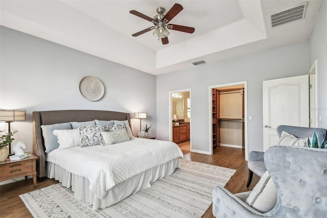 bedroom with a walk in closet, a raised ceiling, wood finished floors, and visible vents