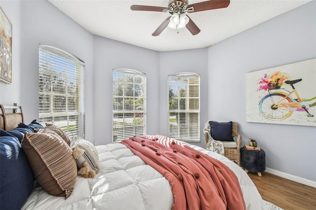 bedroom featuring baseboards, wood finished floors, and a ceiling fan