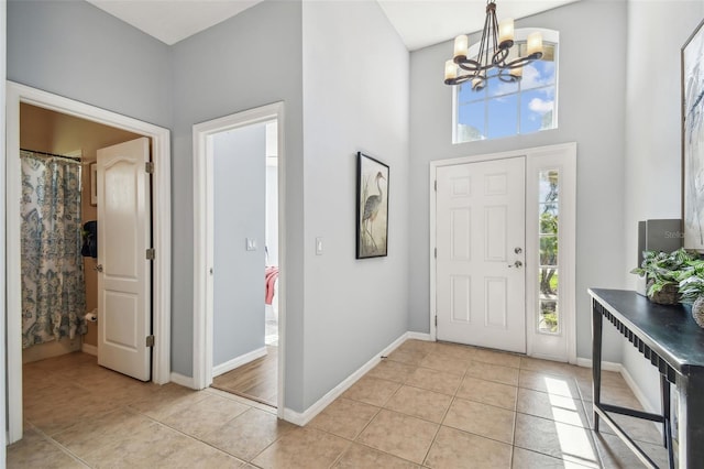 foyer featuring light tile patterned floors, baseboards, a chandelier, and a towering ceiling