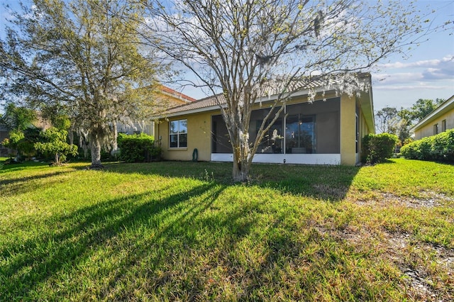 rear view of house featuring stucco siding, a yard, and a sunroom