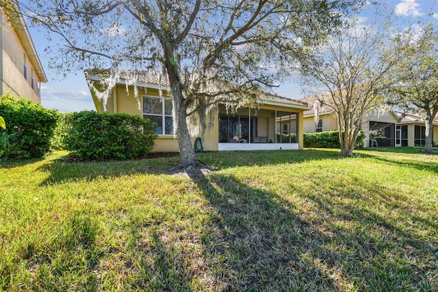 back of property featuring stucco siding, a lawn, and a sunroom