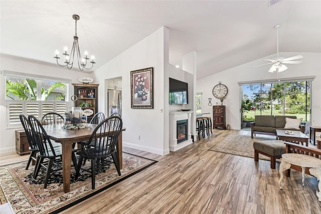 dining area with light wood-type flooring, lofted ceiling, a healthy amount of sunlight, and a glass covered fireplace