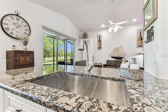 kitchen featuring open floor plan, lofted ceiling, stone counters, a ceiling fan, and a sink