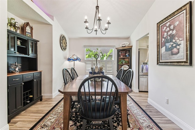 dining room with a notable chandelier, baseboards, and light wood finished floors