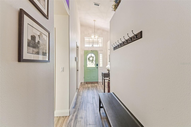 doorway with visible vents, baseboards, wood finished floors, and a chandelier