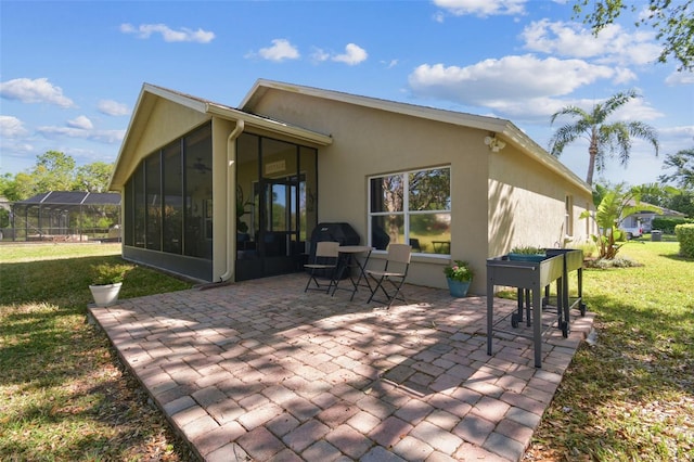 rear view of property with a patio area, a yard, stucco siding, and a sunroom