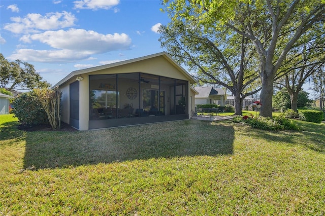 rear view of house featuring stucco siding, a lawn, and a sunroom