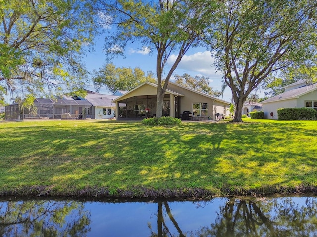 rear view of house featuring stucco siding, a water view, a lawn, and a sunroom