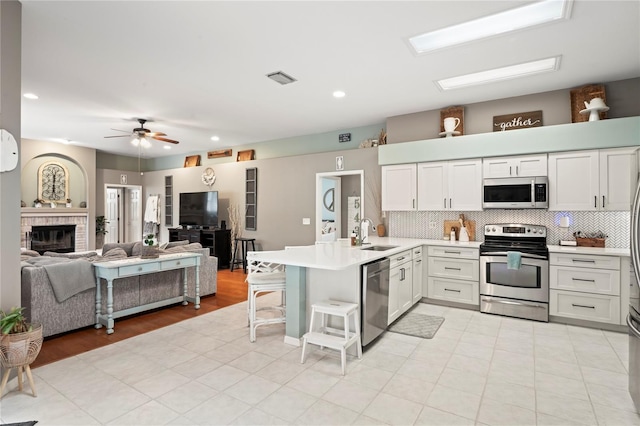 kitchen featuring a sink, appliances with stainless steel finishes, a peninsula, light countertops, and decorative backsplash