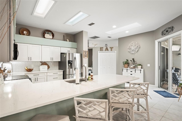 kitchen with a kitchen bar, a sink, tasteful backsplash, a peninsula, and stainless steel fridge with ice dispenser