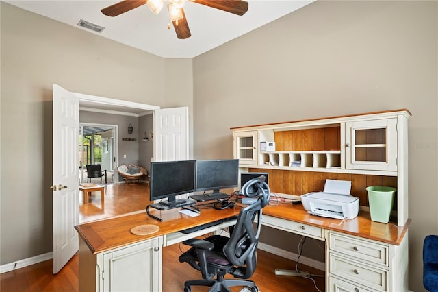 office with visible vents, wood finished floors, built in desk, baseboards, and ceiling fan