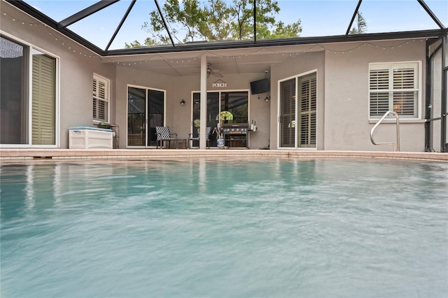 outdoor pool featuring glass enclosure, a patio area, and a ceiling fan