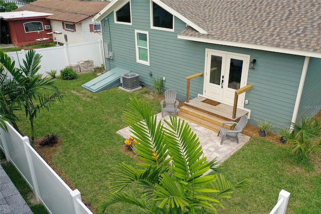 back of house with central AC unit, french doors, a fenced backyard, and roof with shingles