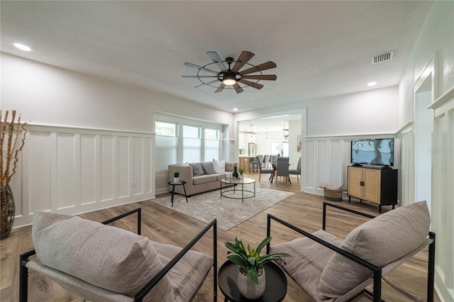 living area featuring visible vents, a wainscoted wall, a ceiling fan, and wood finished floors