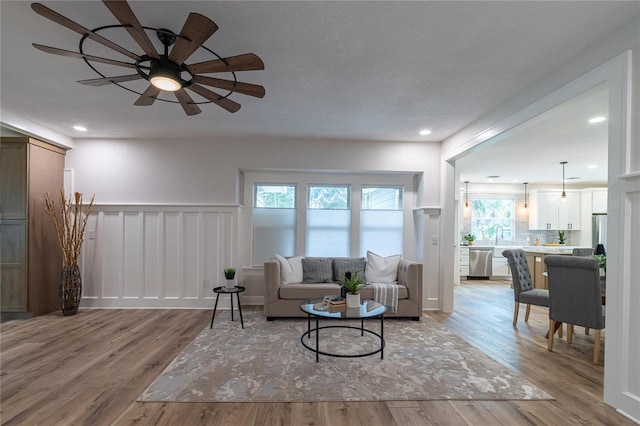 living area featuring light wood-style flooring, recessed lighting, wainscoting, and ceiling fan