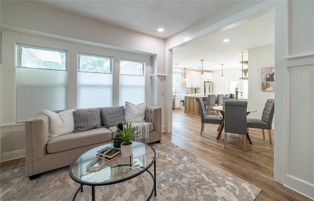 living room with recessed lighting, baseboards, a textured ceiling, and light wood finished floors