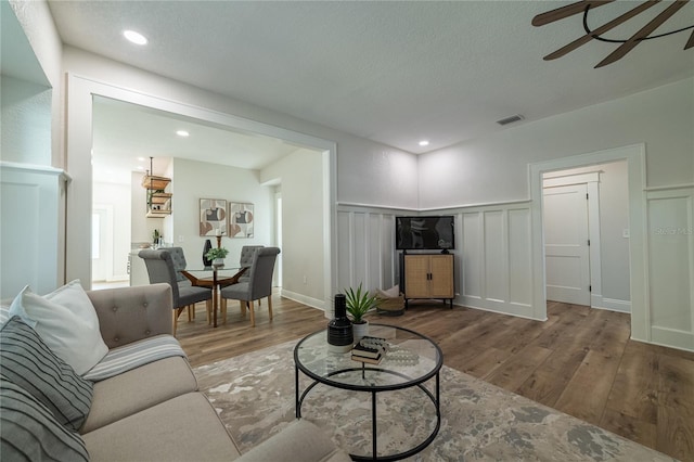 living room with visible vents, wood finished floors, a ceiling fan, and a decorative wall