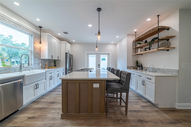 kitchen featuring wood finished floors, a sink, stainless steel appliances, white cabinets, and backsplash