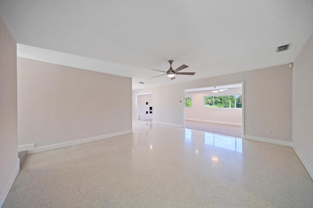 unfurnished room featuring speckled floor, baseboards, visible vents, and ceiling fan