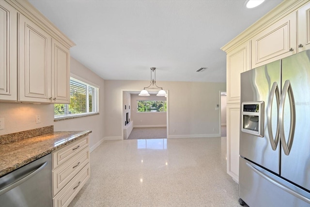 kitchen featuring cream cabinetry, light stone counters, light speckled floor, appliances with stainless steel finishes, and baseboards