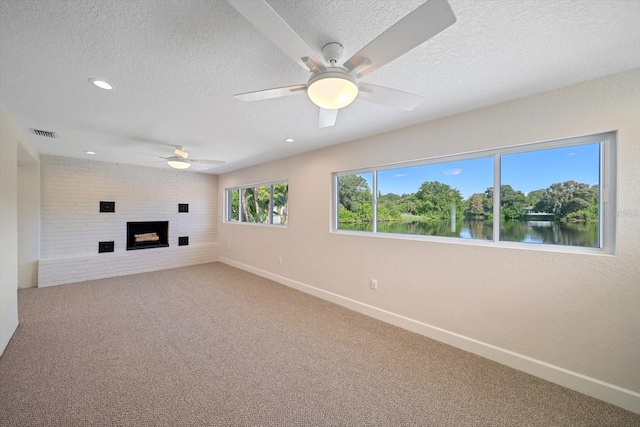 unfurnished living room with visible vents, a brick fireplace, carpet floors, a textured ceiling, and a ceiling fan