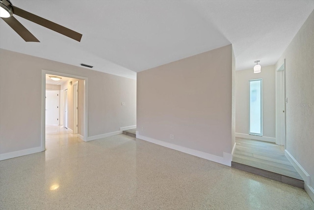 empty room featuring baseboards, visible vents, light speckled floor, and ceiling fan