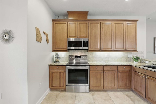 kitchen featuring light stone counters, decorative backsplash, brown cabinets, and appliances with stainless steel finishes