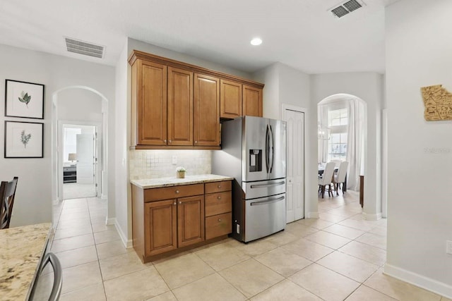 kitchen featuring visible vents, arched walkways, stainless steel refrigerator with ice dispenser, brown cabinets, and backsplash