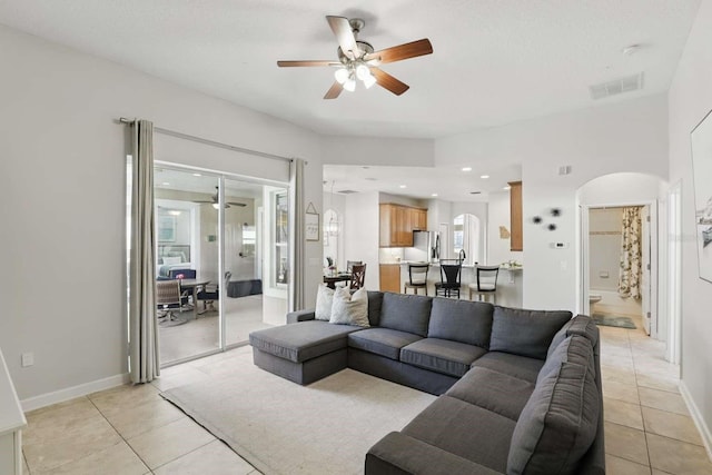 living room with light tile patterned floors, a ceiling fan, visible vents, baseboards, and arched walkways