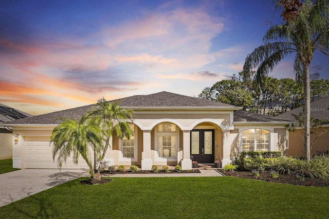 view of front of house featuring a front lawn, concrete driveway, stucco siding, french doors, and an attached garage