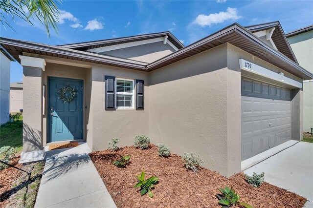 doorway to property with a garage, driveway, and stucco siding